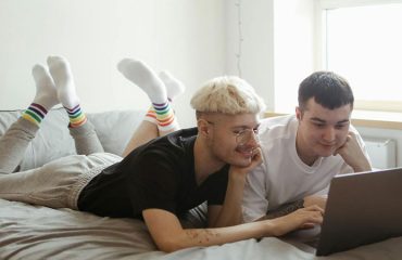 two gay people using a laptop while lying on bed